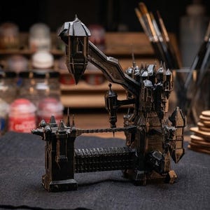 Può includere: Modello dettagliato di un castello in miniatura nero con più torri, torrette e un ponte. Il modello presenta intricati dettagli architettonici ed è ambientato su uno sfondo sfocato di materiali artistici.