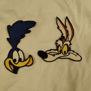 May include: Two embroidered cartoon patches, one of a blue Road Runner and one of a brown Wile E. Coyote.