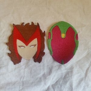 May include: Two embroidered patches featuring the faces of Scarlet Witch and Vision from the Marvel Cinematic Universe. Scarlet Witch's patch is red, white, and brown, while Vision's patch is green, red, and yellow.