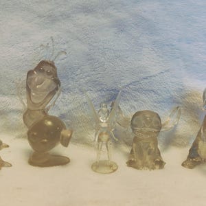 Puede incluir: Cinco figuritas de pl&aacute;stico transparente de personajes populares de Disney. Los personajes incluyen a Olaf de Frozen, Campanilla, Stitch y dos versiones del drag&oacute;n de Mulan.