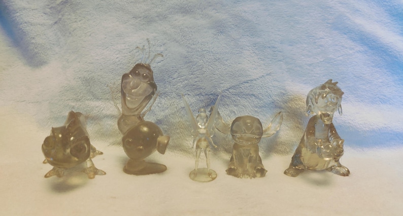 Puede incluir: Cinco figuritas de pl&aacute;stico transparente de personajes populares de Disney. Los personajes incluyen a Olaf de Frozen, Campanilla, Stitch y dos versiones del drag&oacute;n de Mulan.