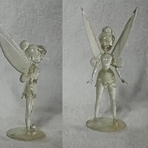 Puede incluir: Una figurita de cristal transparente de Campanita, el hada de la pel&iacute;cula de Disney Peter Pan. La figurita est&aacute; posada con las alas extendidas y los brazos extendidos. La figurita mide aproximadamente 15 cm de alto.
