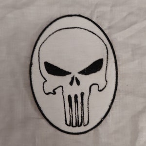 May include: White embroidered patch featuring a black skull and crossbones design. The skull has a menacing expression with two black eye sockets.