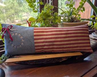 May include: A rectangular throw pillow featuring a blue denim section with a circle of embroidered stars and a red and white striped section. A red and white fabric tie is attached to the top left corner. A wooden ruler measuring 30 cm is placed in front.