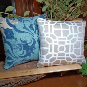 Peut inclure: Deux coussins d&eacute;coratifs. L'un pr&eacute;sente un motif floral bleu et turquoise. L'autre a un motif g&eacute;om&eacute;trique blanc et gris. Les deux coussins sont carr&eacute;s et semblent &ecirc;tre en tissu.