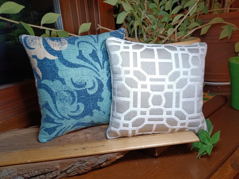 Peut inclure: Deux coussins d&eacute;coratifs. L'un pr&eacute;sente un motif floral bleu et turquoise. L'autre a un motif g&eacute;om&eacute;trique blanc et gris. Les deux coussins sont carr&eacute;s et semblent &ecirc;tre en tissu.