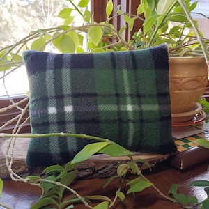 May include: A rectangular fleece pillow featuring a dark green, black, and white plaid pattern. The fabric has a soft, textured surface with a classic tartan design consisting of intersecting horizontal and vertical lines in varying shades.