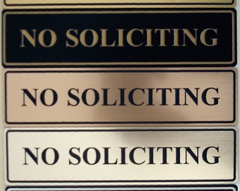 May include: Five different versions of a "No Soliciting" sign. The signs are made of metal and have a gold, black, or beige finish. The text is in black or white.