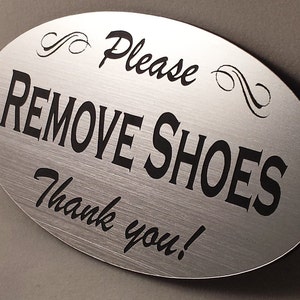 May include: Oval-shaped brushed silver sign with black text that reads "Please Remove Shoes Thank you!"