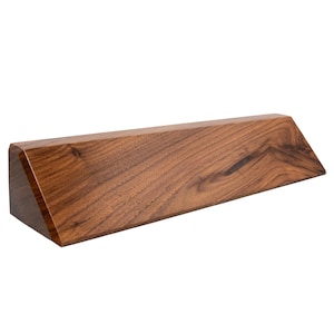 May include: A wedge-shaped wooden block with a smooth, polished finish and a prominent dark brown wood grain pattern. The object features a flat rectangular front face, a slanted top surface, and a triangular side profile with sharp edges.