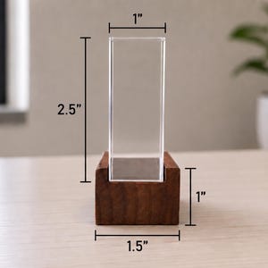 Op de afbeelding: Een doorzichtige rechthoekige acryl displayhouder in een donkerbruine houten voet. De acryl behuizing is 6,35 cm hoog en 2,54 cm breed. De houten voet is 2,54 cm hoog en 3,81 cm breed en is voorzien van een centrale gleuf.