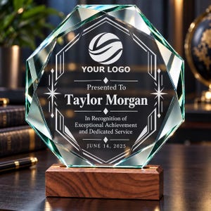 May include: An octagonal clear glass award plaque with beveled edges, mounted on a rectangular dark wood base. The glass features an etched logo, the text "Presented To Taylor Morgan," "In Recognition of Exceptional Achievement and Dedicated Service," and "JUNE 14, 2025."