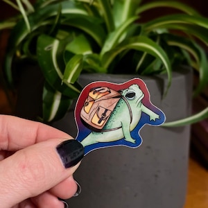 May include: A green frog with a brown backpack on its back. The frog is cartoon-style and has a happy expression. The background is a gradient of red, blue, and purple.