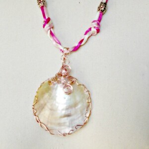 May include: A pink and white braided cord necklace with silver beads and a large, iridescent seashell pendant wrapped in copper wire.