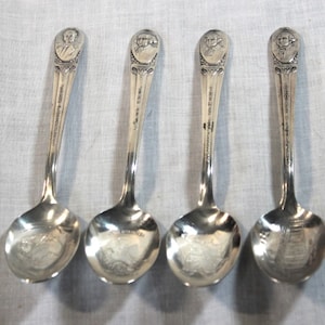 May include: Set of four silver spoons featuring a design of a president's head on the handle and a scene on the bowl. The spoons are in good condition with no visible damage.