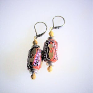 May include: A pair of dangle earrings with red and gold geometric patterned beads and silver wire accents. The earrings have silver hooks.