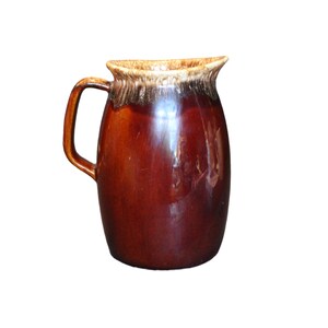 May include: A brown ceramic pitcher with a glazed finish. The pitcher has a wide mouth and a handle.