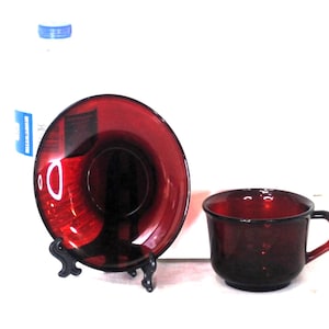 Op de afbeelding: Een set van twee robijnrode glazen theekopjes en schoteltjes. Het kopje en het schoteltje zijn beide diep rood van kleur en hebben een glanzende afwerking.