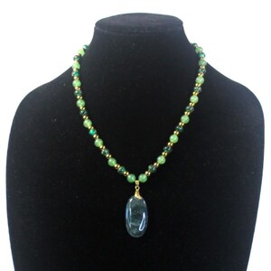 May include: A green and gold beaded necklace with a large oval green gemstone pendant.