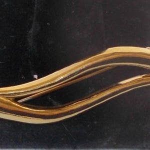 Pu&ograve; includere: Un fermaglio dorato con un design ondulato e due accenti di perle finte.