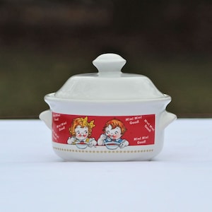 May include: White ceramic soup tureen with a lid, featuring a red and white illustration of two children eating soup. The illustration includes the text "M'm! M'm! Good!"