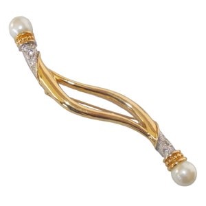 Pu&ograve; includere: Un fermaglio dorato con due perle finte e un design a spirale. Le perle sono incastonate in montature dorate e il fermaglio &egrave; decorato con strass trasparenti.