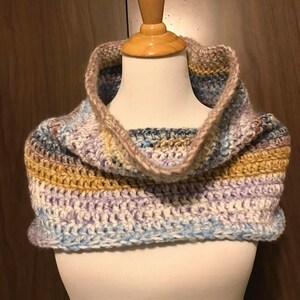 May include: A crocheted cowl in shades of blue, purple, brown, and beige. The cowl has a wide, folded-over collar.