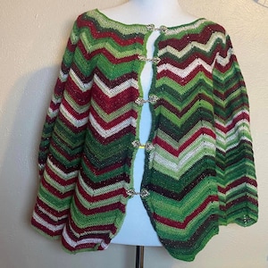 May include: A green, red, and white crocheted poncho with silver buttons down the front.