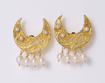 May include: A pair of gold-toned crescent moon earrings with a textured surface, inlaid with small clear crystals and white pearls. Each earring features four dangling white pearls suspended from the bottom edge of the crescent shape.
