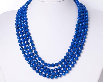 May include: A multi-strand necklace featuring four rows of vibrant, deep blue spherical beads. The beads are uniform in size and color, creating a layered effect that drapes around the neck. The necklace is displayed on a plain white bust.