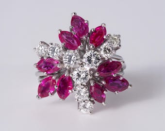 May include: A silver-toned ring featuring a cluster of marquise-cut vibrant pink stones and round brilliant-cut clear stones arranged in a floral pattern. The metal setting holds the stones in a dense, multi-layered design that radiates outward.
