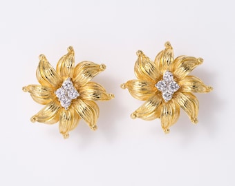 May include: A pair of gold earrings shaped like blooming flowers with textured petals. Each earring features a cluster of four small, clear, round-cut stones set in the center, creating a bright, reflective focal point against the yellow gold.