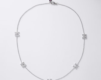 May include: A silver-toned chain necklace featuring five evenly spaced letter M charms. Each letter M is encrusted with small, clear, sparkling stones. The necklace includes a delicate link chain and a small clasp closure at the top center.