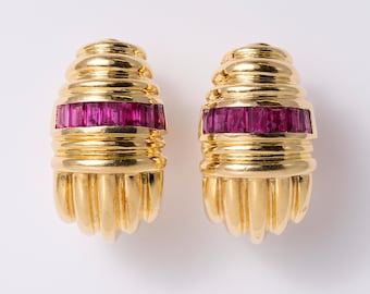 May include: A pair of gold-toned earrings featuring a ribbed, dome-shaped top and a vertical fluted base. Each earring is accented with a horizontal band of rectangular, deep pink-red gemstones set across the center of the metallic structure.