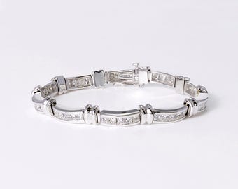 May include: A silver-toned metal link bracelet featuring a series of channel-set square-cut clear stones. The design alternates between smooth metal segments and sections embedded with stones, secured by a rectangular box clasp mechanism.