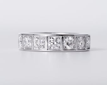 May include: A silver-toned band ring featuring a series of round, clear, faceted stones set within individual square metal frames that span the entire circumference of the band, creating a continuous channel-like design with a polished finish.