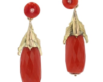 May include: A pair of gold earrings featuring red coral and small diamonds. Each earring has a round red coral stud, a gold leaf-like design, and a faceted, teardrop-shaped red coral pendant. The earrings are displayed against a white background.