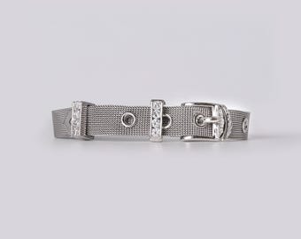 May include: A silver-toned mesh bracelet designed to resemble a belt, featuring a buckle closure, two metal loops embedded with small clear stones, and additional circular metal eyelets along the band for a structured, metallic appearance.
