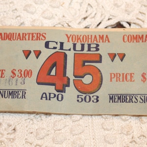 May include: Vintage Yokohama Club 45 ticket. The ticket features the text "HEADQUARTERS YOKOHAMA COMMAND CLUB 45" in red and blue. The price is $3.00. The book number is 01613 and APO 503. The ticket is on a light beige background.