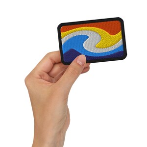 Op de afbeelding: Een kleurrijk geborduurd patch met een golfontwerp. De golf is blauw, wit en geel, en de achtergrond is oranje en rood. Het patch is omgeven door een zwarte rand.