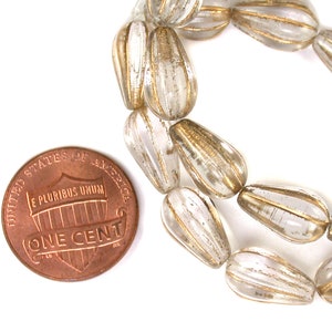 May include: A strand of clear glass beads with gold accents. The beads are teardrop shaped and have a striated texture. The beads are about the size of a UK penny.