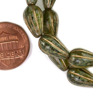 May include: Green and gold glass beads with a speckled pattern. The beads are shaped like teardrops and are about the size of a UK penny.