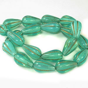 May include: A strand of teal blue glass beads with gold accents. The beads are shaped like teardrops and have a textured surface.
