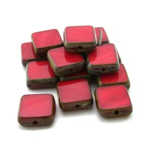 May include: A pile of red square ceramic beads with a brown and green glaze. The beads have a hole in the center for stringing.