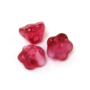 May include: Three pink glass flower-shaped beads with a translucent finish.