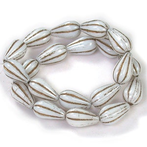 May include: A strand of white glass beads with gold stripes. The beads are teardrop shaped.