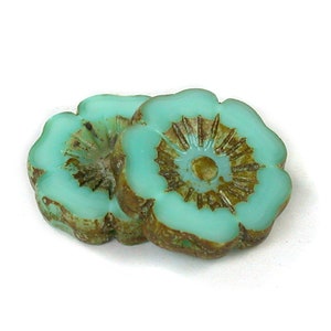 May include: Two turquoise blue glass flower-shaped beads with brown centers. The beads have a raised, textured design.