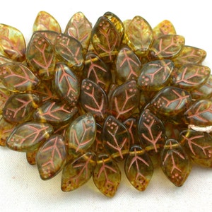 May include: A collection of green glass leaf beads with a copper-colored design. The beads are arranged in a loose pile.