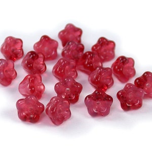 Puede incluir: Un grupo de 17 cuentas de vidrio de color rosa en forma de flor. Las cuentas son translúcidas y tienen un acabado ligeramente iridiscente.