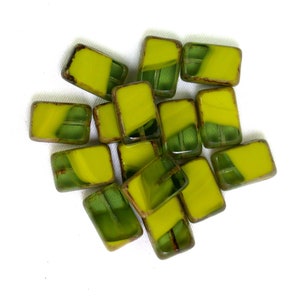 May include: A collection of rectangular glass beads. Each bead features a vibrant yellow and green color scheme with a textured appearance. The beads have a dark brown border, creating a distinct contrast against the bright colors.